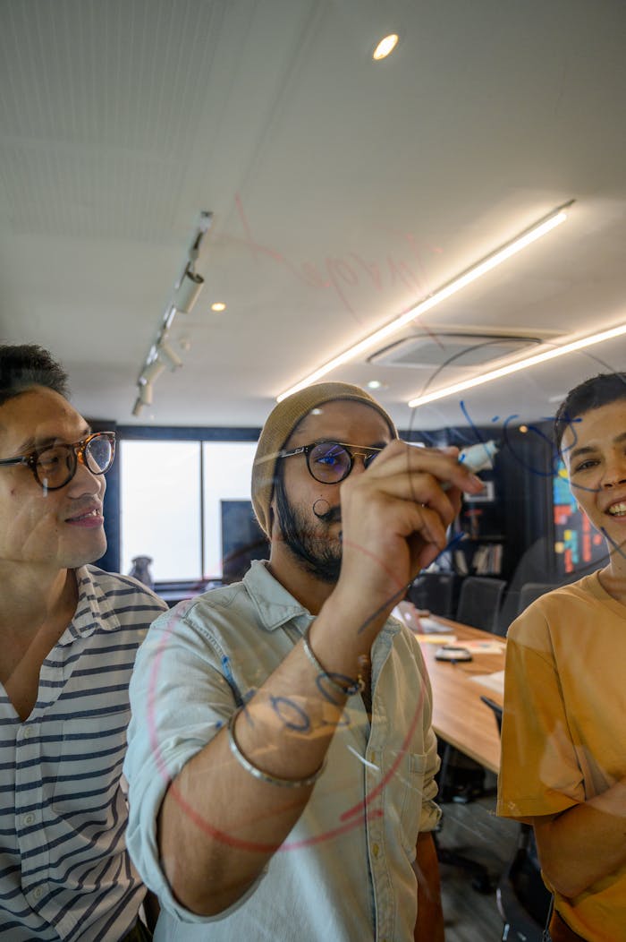 Three adults engaging in a collaborative discussion in a modern office, sketching ideas on a glass board.